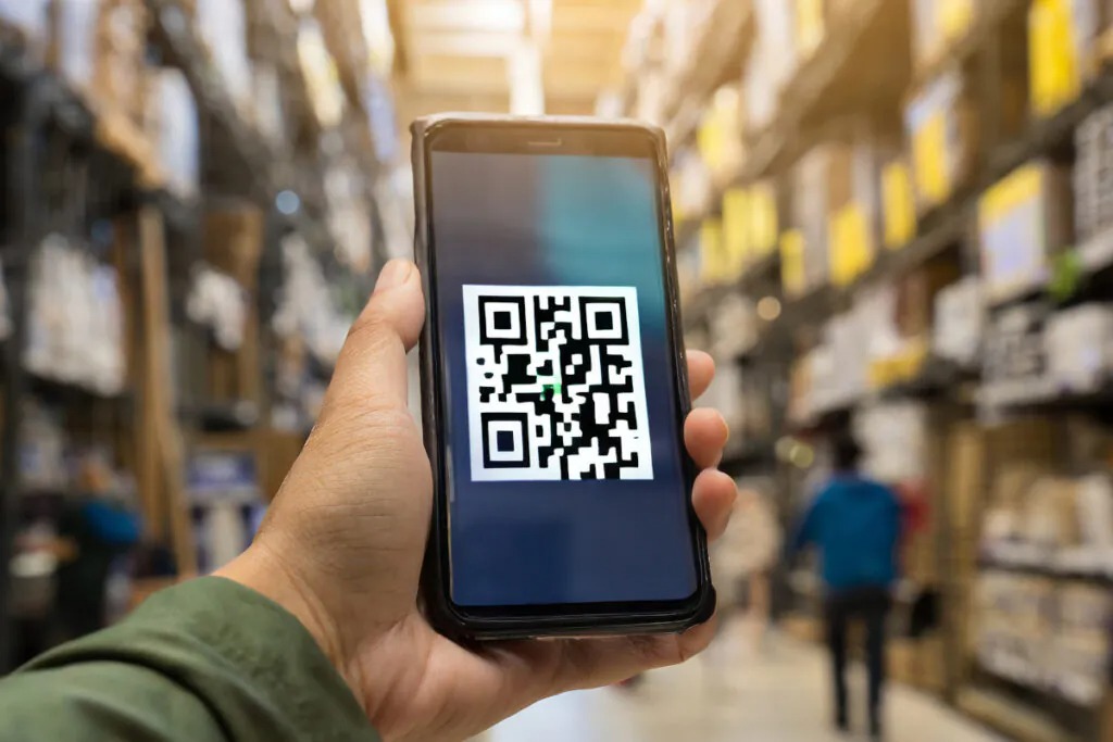 Cliente utiliza smartphone para escanear QR code em gôndola de varejo, acessando detalhes técnicos e vídeos informativos sobre o produto.