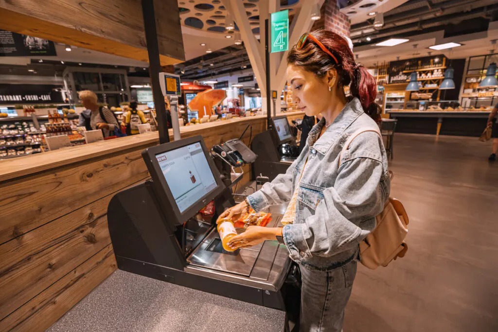Terminal de autoatendimento moderno em ambiente de varejo phygital, focado na agilidade do checkout e na autonomia da jornada de compra.